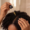 Woman applying Atorisé hair growth oil to scalp with dropper