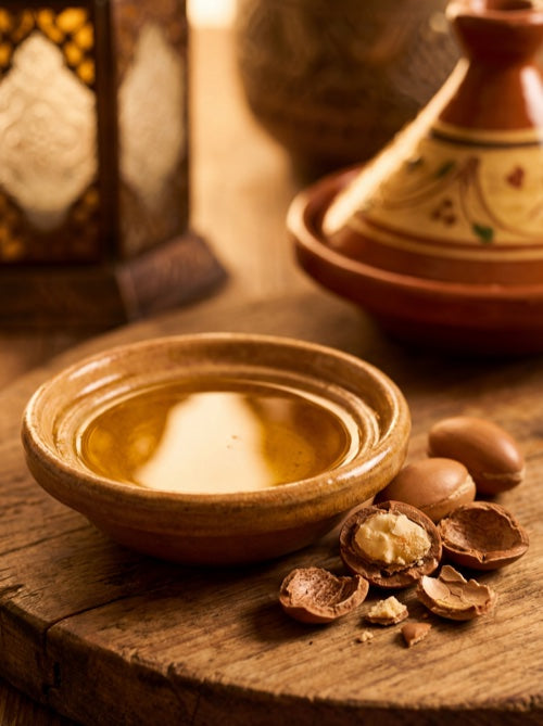 Golden argan oil in ceramic bowl with cracked argan nuts