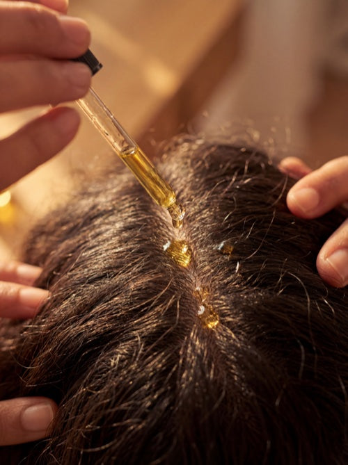 Golden oil drops being applied to scalp from glass dropper