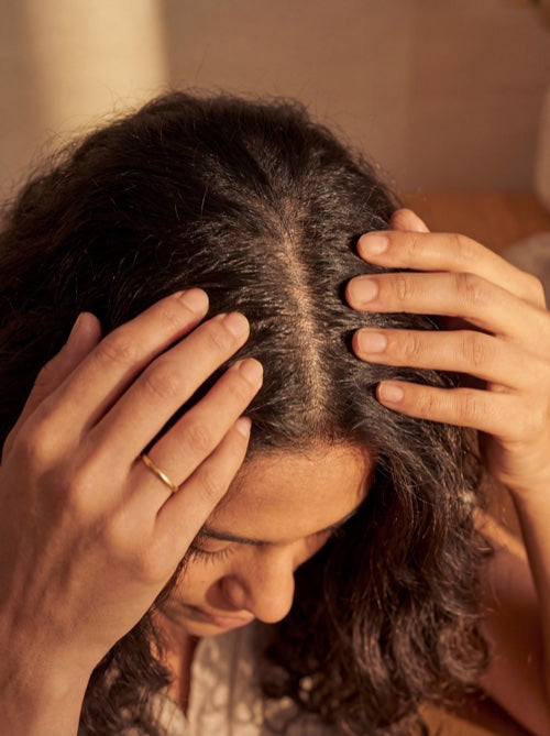 Fingertips massaging oil into scalp in circular motions
